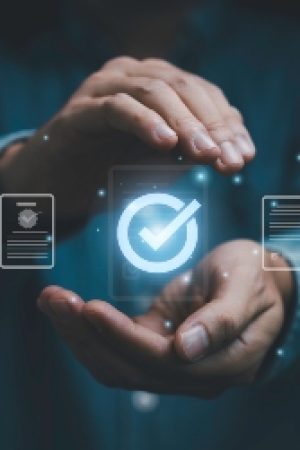 Quality assurance and certification concept with hands protecting digital approval checkmark and compliance documents. Symbol of quality control, verification, standards and business trust.